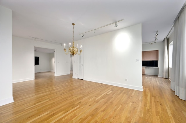 spare room with light wood-type flooring, baseboards, a notable chandelier, and track lighting