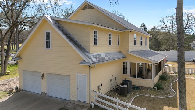 rear view of house featuring central air condition unit, concrete driveway, an attached garage, metal roof, and fence