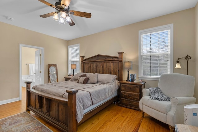 bedroom with multiple windows, light wood-style flooring, baseboards, and ensuite bathroom