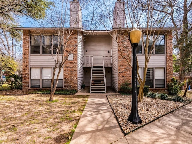 view of front of house featuring a chimney, brick siding, and stairway