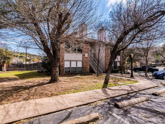 view of front of property with brick siding, stairway, a chimney, and fence