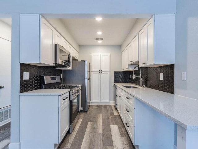 kitchen featuring backsplash, appliances with stainless steel finishes, white cabinetry, a sink, and wood finished floors