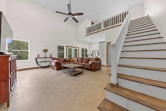 living area featuring a towering ceiling, stairs, concrete floors, and baseboards