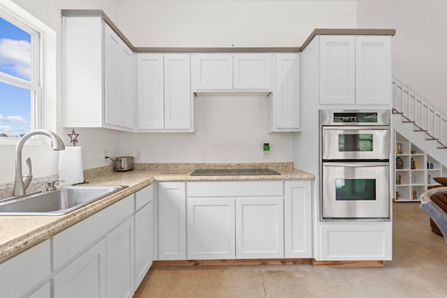 kitchen featuring white cabinets, double oven, black electric cooktop, and a sink