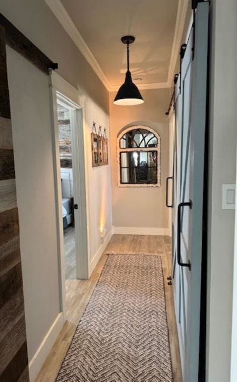 hallway featuring light wood-type flooring, a barn door, ornamental molding, and baseboards