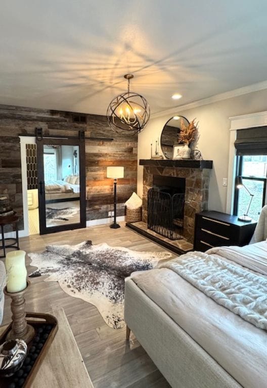 bedroom with ornamental molding, wood finished floors, an inviting chandelier, a stone fireplace, and wood walls