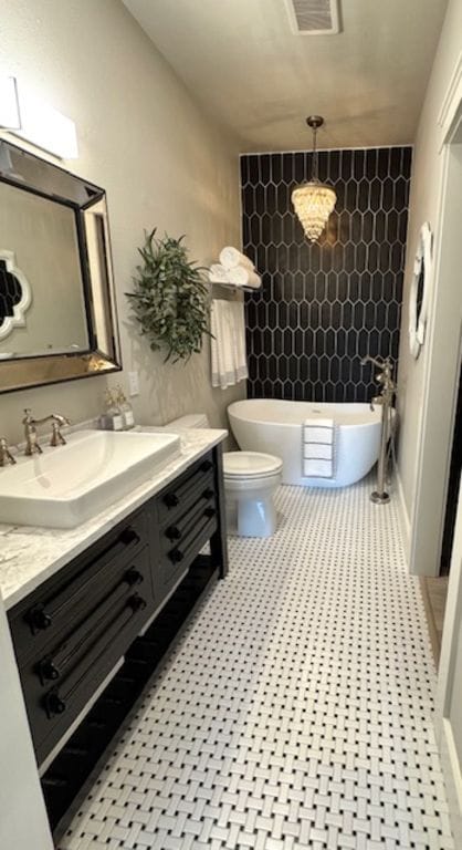 bathroom with a soaking tub, visible vents, vanity, and toilet