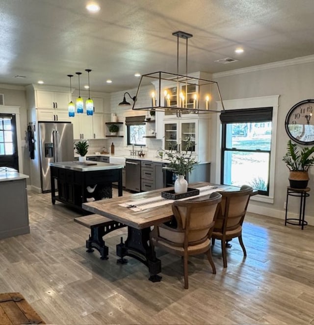 dining area with baseboards, light wood finished floors, a textured ceiling, and crown molding