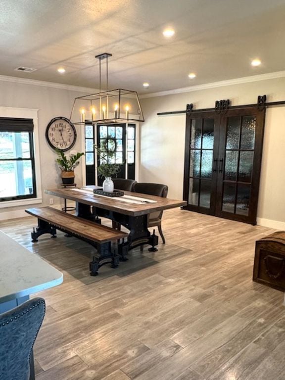 dining area with an inviting chandelier, ornamental molding, a barn door, wood finished floors, and baseboards