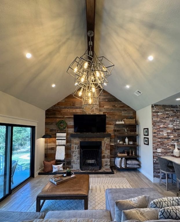 living area featuring high vaulted ceiling, visible vents, a stone fireplace, and wood finished floors