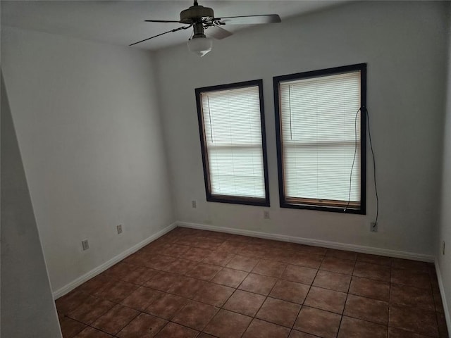 tiled empty room with ceiling fan and baseboards