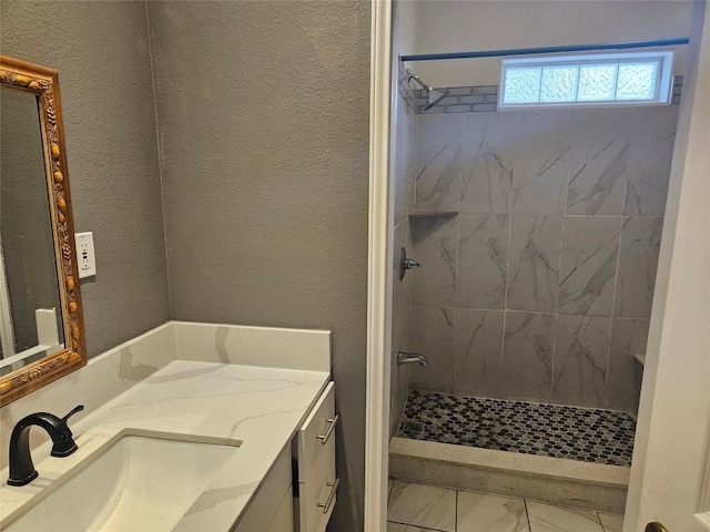 bathroom with marble finish floor, a textured wall, tiled shower, and vanity