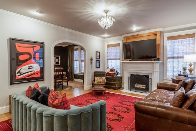 living area featuring a fireplace with flush hearth, arched walkways, wood finished floors, and ornamental molding