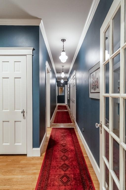 hallway featuring french doors, ornamental molding, wood finished floors, and baseboards