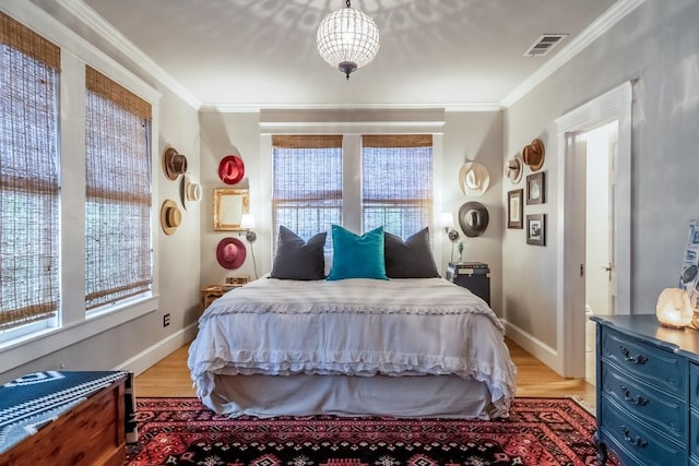 bedroom with light wood-style flooring, visible vents, baseboards, and ornamental molding