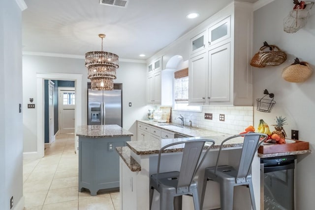 kitchen with light stone counters, a kitchen island, stainless steel fridge with ice dispenser, tasteful backsplash, and crown molding