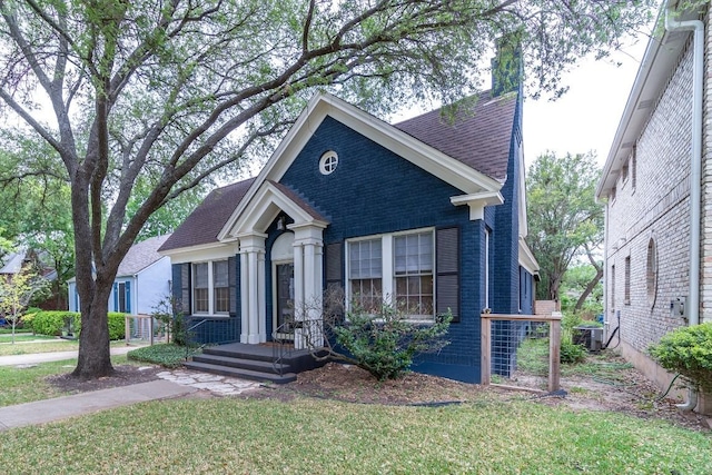 view of front of house featuring a shingled roof, a front yard, brick siding, and central air condition unit