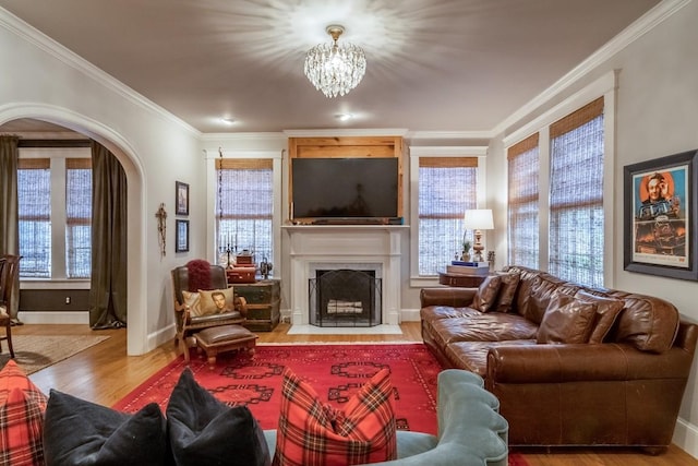 living room with arched walkways, crown molding, a fireplace with flush hearth, wood finished floors, and baseboards