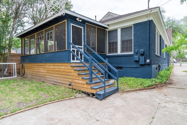 view of front of house with a patio, brick siding, fence, a sunroom, and stairway