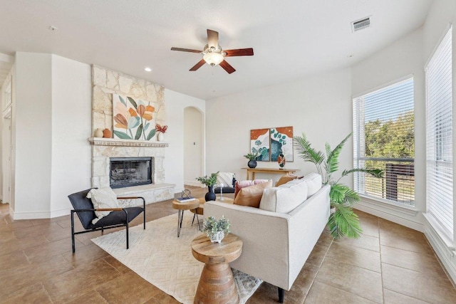 living area featuring arched walkways, ceiling fan, tile patterned flooring, a fireplace, and visible vents