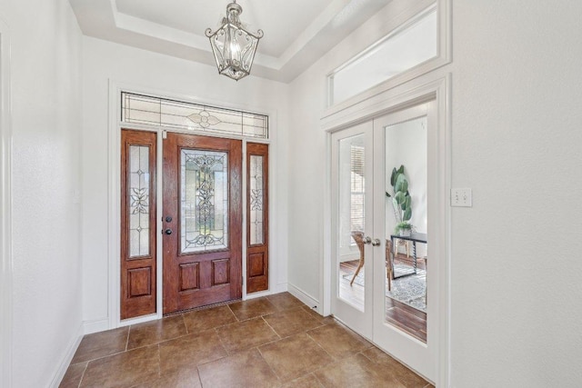 entryway with baseboards, a tray ceiling, a notable chandelier, and french doors