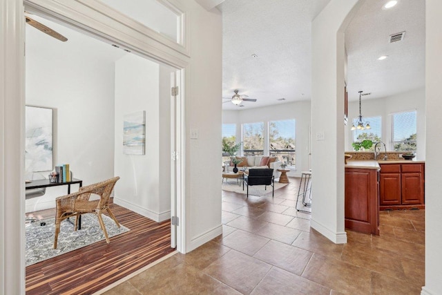 hallway featuring arched walkways, recessed lighting, a sink, visible vents, and baseboards