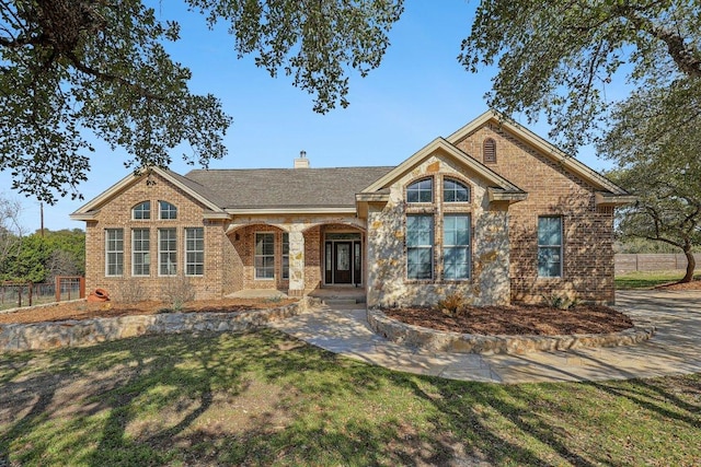 view of front of house featuring a porch, brick siding, fence, a chimney, and a front yard