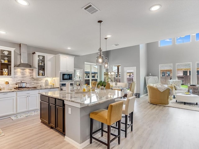 kitchen featuring stainless steel appliances, visible vents, light wood-style floors, wall chimney range hood, and backsplash