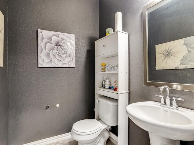 half bath with a textured wall, baseboards, a sink, and toilet