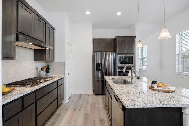 kitchen featuring a kitchen island with sink, stainless steel appliances, a sink, light wood-style floors, and decorative backsplash