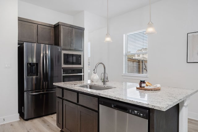 kitchen featuring a center island with sink, stainless steel appliances, light wood-style floors, a sink, and dark brown cabinets