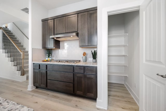 1409 Kneehigh Ln, Georgetown, TX 78633 - kitchen with under cabinet range hood, stainless steel gas cooktop, dark brown cabinets, and light wood finished floors