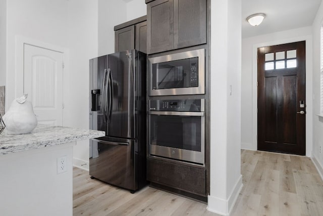 kitchen featuring dark brown cabinetry, baseboards, light wood-style flooring, light stone counters, and stainless steel appliances