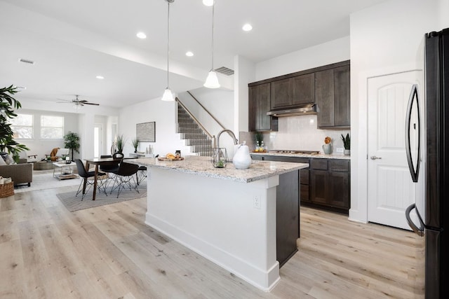 1409 Kneehigh Ln, Georgetown, TX 78633 - kitchen with freestanding refrigerator, dark brown cabinets, backsplash, under cabinet range hood, and recessed lighting