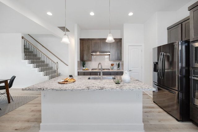 1409 Kneehigh Ln, Georgetown, TX 78633 - kitchen featuring refrigerator with ice dispenser, under cabinet range hood, dark brown cabinetry, tasteful backsplash, and light stone countertops