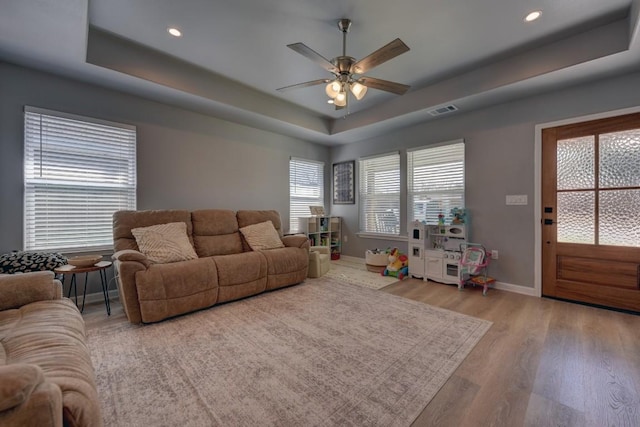 living room featuring wood finished floors, a raised ceiling, visible vents, and baseboards