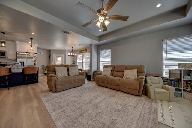 living room featuring a tray ceiling, recessed lighting, visible vents, light wood-style flooring, and ceiling fan with notable chandelier