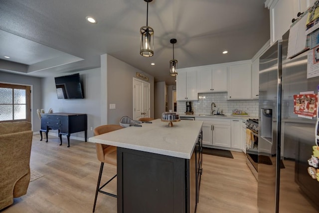 kitchen featuring a sink, white cabinets, light wood finished floors, tasteful backsplash, and a kitchen bar