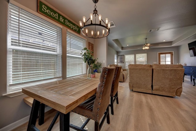 dining room featuring light wood-style floors, a tray ceiling, visible vents, and baseboards