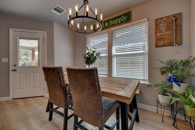 dining space with baseboards, visible vents, light wood finished floors, and an inviting chandelier