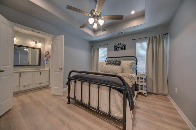 bedroom with a raised ceiling, visible vents, light wood-style flooring, and baseboards