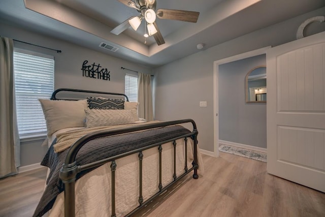 bedroom with arched walkways, visible vents, baseboards, light wood finished floors, and a raised ceiling