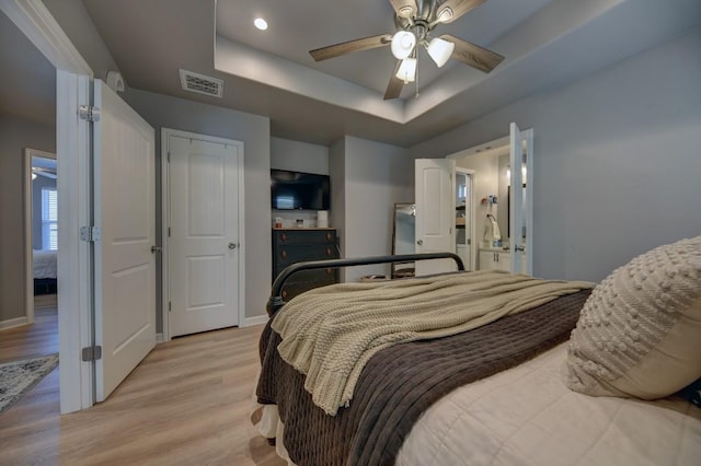 bedroom with a raised ceiling, visible vents, light wood-style flooring, ceiling fan, and baseboards