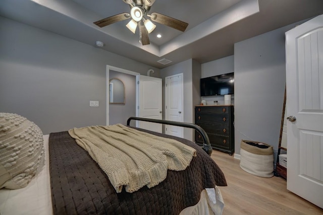 bedroom featuring ceiling fan, light wood finished floors, a raised ceiling, and visible vents