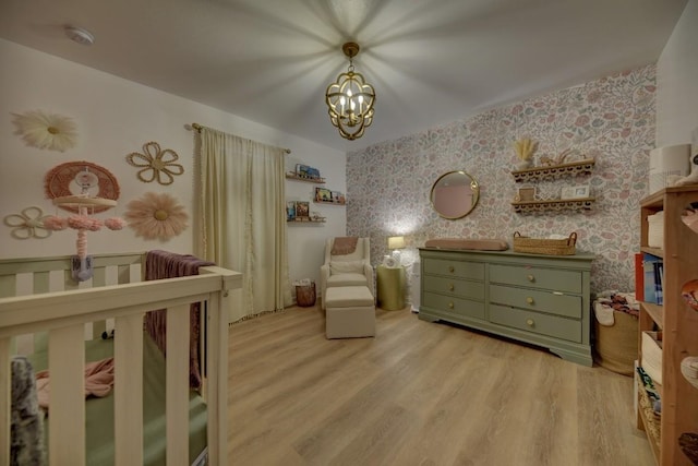 bedroom featuring a chandelier, a crib, light wood-style floors, and wallpapered walls