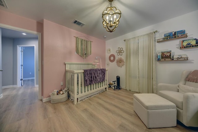 bedroom featuring a notable chandelier, wood finished floors, visible vents, baseboards, and a nursery area