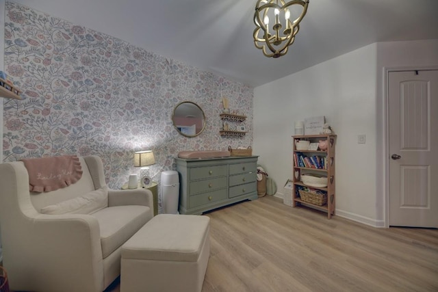 sitting room featuring wallpapered walls, baseboards, an accent wall, wood finished floors, and a notable chandelier