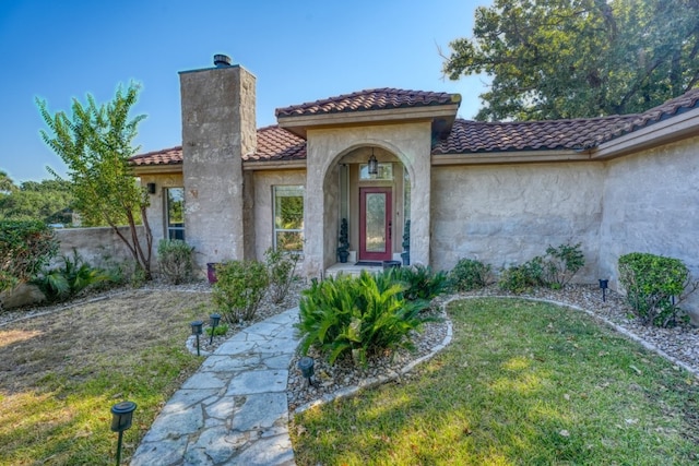 view of exterior entry featuring a chimney, a tile roof, a lawn, and stucco siding