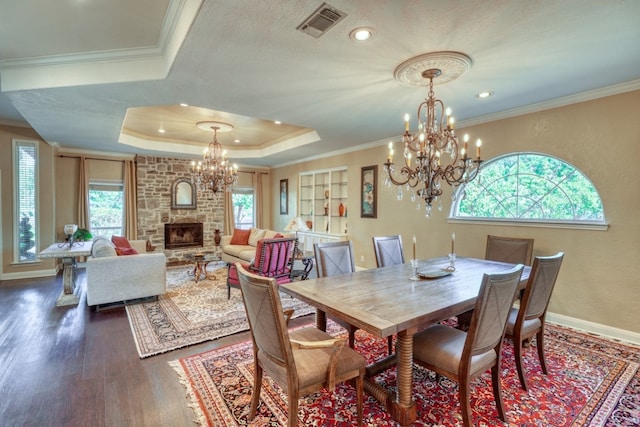 dining area with a chandelier, a large fireplace, ornamental molding, a tray ceiling, and dark wood finished floors