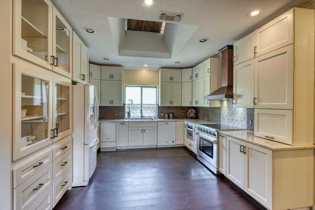 kitchen featuring white appliances, visible vents, decorative backsplash, a raised ceiling, and wall chimney range hood